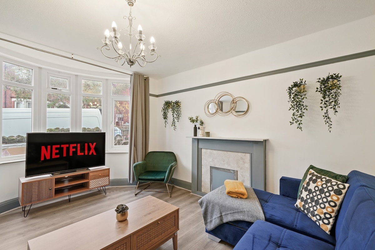 Living room with a blue sofa, green armchair, bay window and chandelier