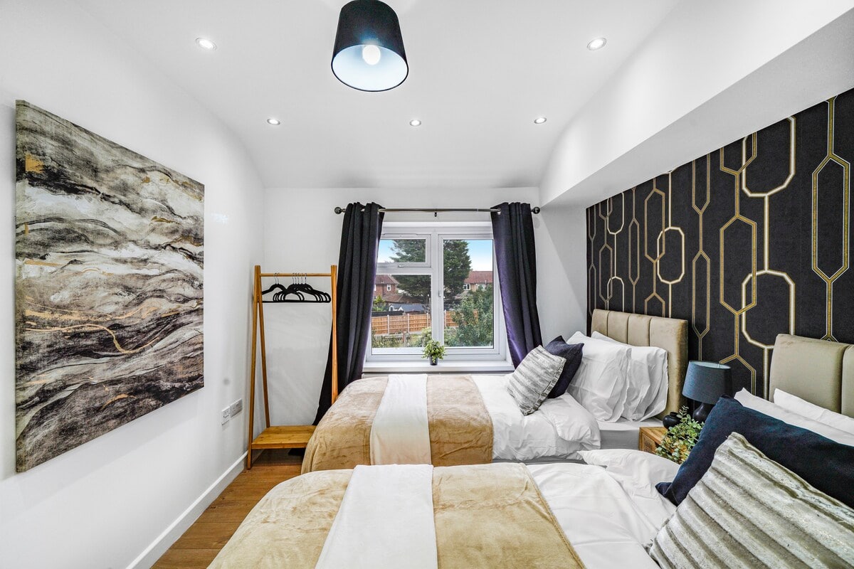 Twin bedroom with upholstered headboards, black and gold patterned wallpaper and dark curtains