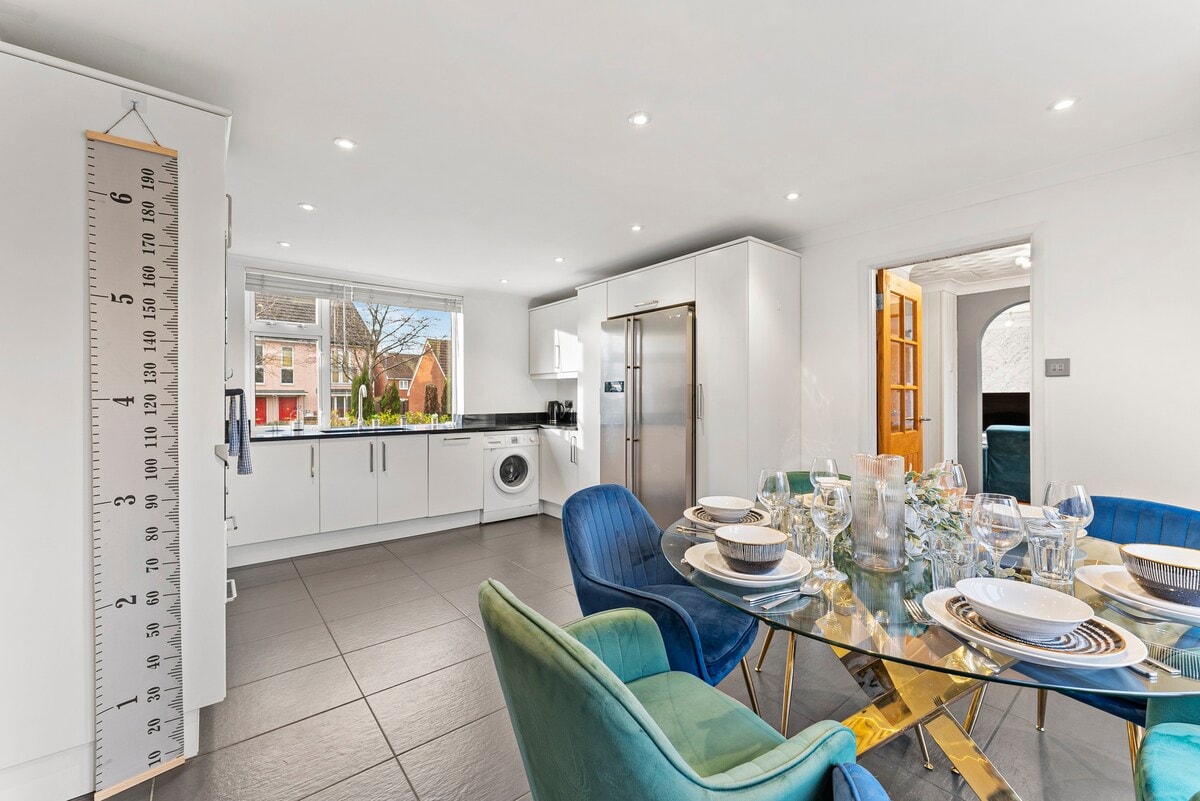 Open-plan white kitchen and dining area with a glass table and blue and green chairs