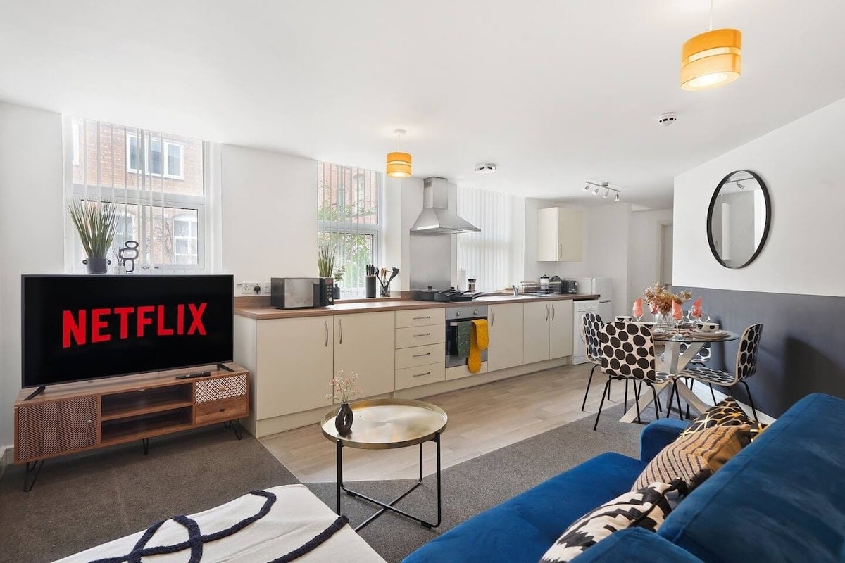 Open-plan living room with a blue sofa, white kitchen and round dining table