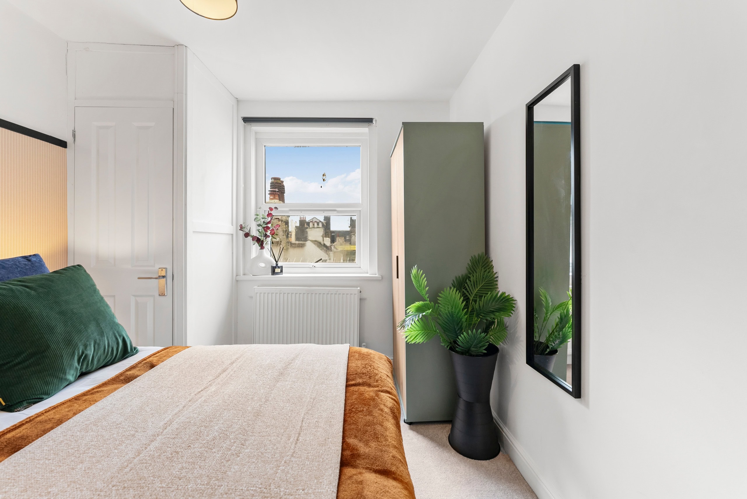 Bedroom with green cushions, a green wardrobe, wall mirror and potted plant