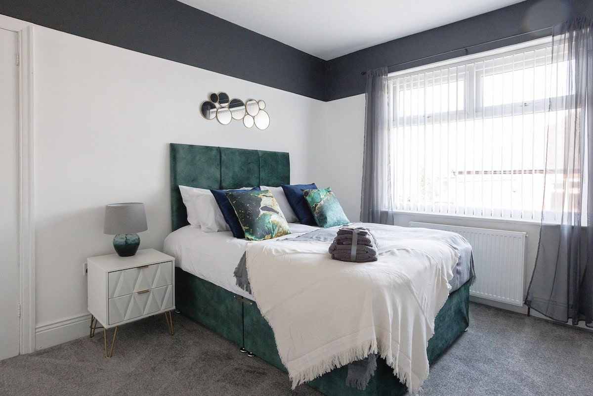 Double bedroom with a green upholstered bed, white linen and a large window